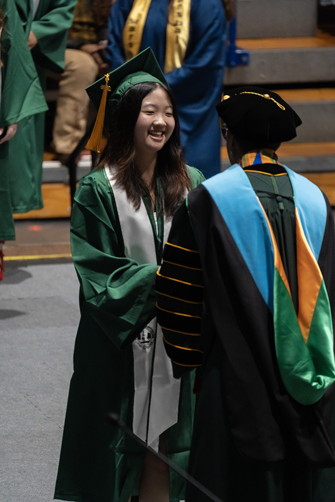 A smiling Frederick Community College graduate in a cap and gown posing with their diploma cover.