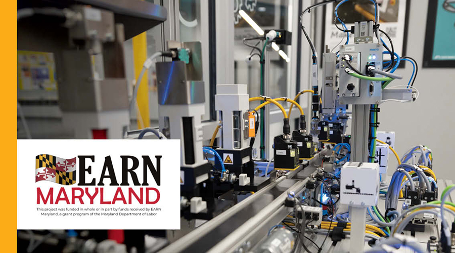 An automated industrial workspace features intricate machinery with wires, sensors, and mechanical components organized on a production line. A white overlay in the bottom-left corner displays the 