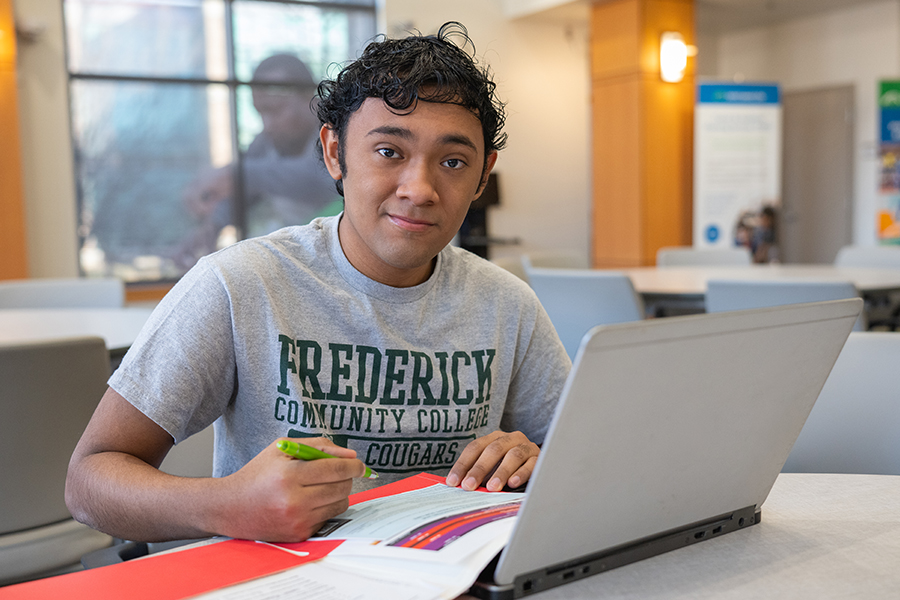 smiling student with fcc shirt sitting at table with laptop