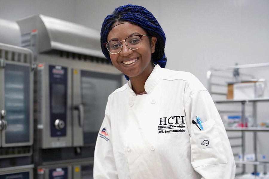 HCTI culinary student in white chef coat smiling in a commercial kitchen